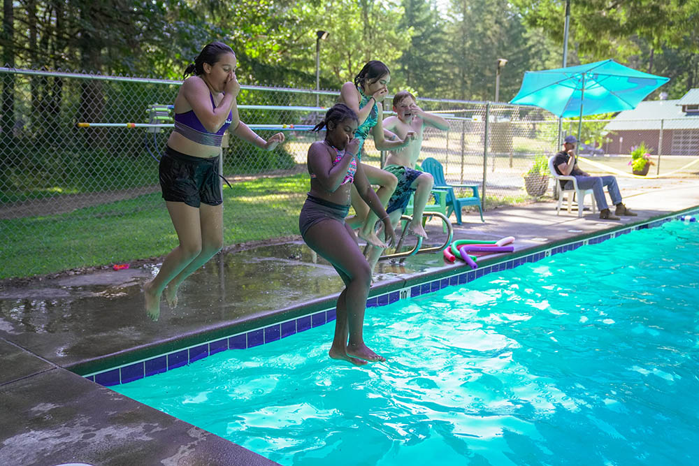 Four campers jumping into the pool from the side at Camp Lutherwood Oregon