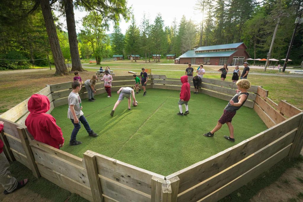 Youth campers playing gaga ball at Camp Lutherwood Oregon with the back field and dining hall in the background.