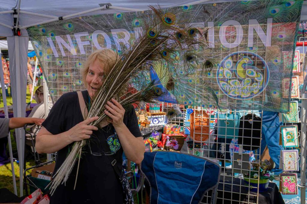 A woman holding peacock feather at a festival.