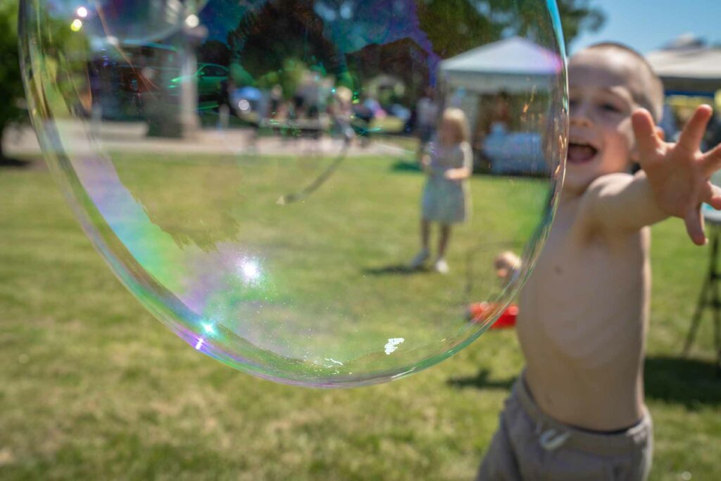 A boy reaching for a large bubble in the park.